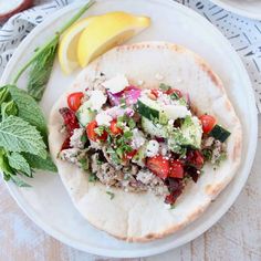 a taco with meat, tomatoes and cucumbers on it next to a lemon wedge