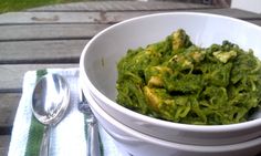 a white bowl filled with green pasta on top of a table next to silverware