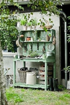 a green shelf with pots and plants on it in the grass next to a tree