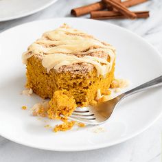 a white plate topped with a piece of cake next to a fork and cinnamon sticks