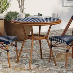 two chairs and a table on a stone patio with potted plants in the background