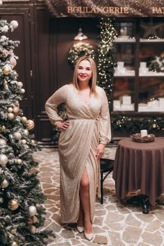 a woman standing in front of a christmas tree wearing a gold dress and tan slippers