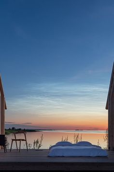 a bed sitting on top of a wooden platform next to a body of water at sunset