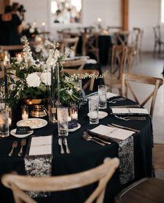 the table is set with black linens and white flowers, candles, and place settings