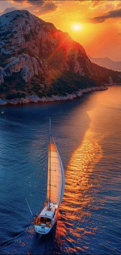 a sailboat in the water at sunset with mountains in the backgrouund