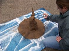 a woman sitting on the ground painting a hat