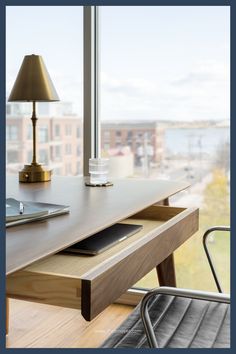 a wooden desk with a laptop on it next to a lamp and window overlooking the city