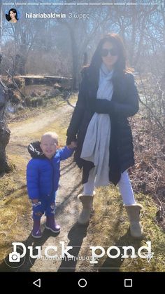 a woman holding the hand of a small child on a dirt path with trees in the background