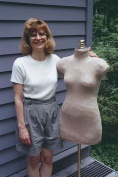 a woman standing next to a mannequin on a wooden platform in front of a house