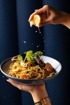 someone is sprinkling lemon over a plate of pasta with shrimp and basil on top