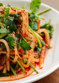 a white plate topped with noodles and veggies covered in seasoning on top of a wooden table