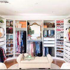 an organized closet with white furniture and lots of clothes on shelves in the middle of it