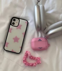 an iphone case, headphones, and hair tie laying on a white sheet with pink stars