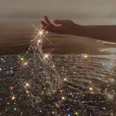 a person's hand reaching out over the water with sparkling lights on it and in the background