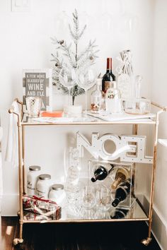 a bar cart with wine glasses and bottles on it in front of a christmas tree