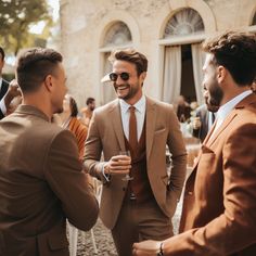 three men in suits talking to each other at an outdoor event, one wearing sunglasses and the other smiling