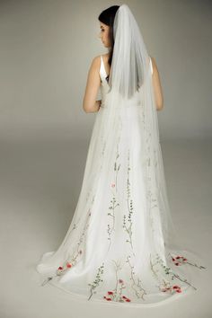 a woman in a white wedding dress with red flowers on the back and veil over her head