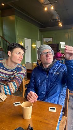 two men sitting at a table in a restaurant, one holding up a small card