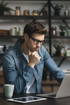 a man sitting in front of a laptop computer on top of a wooden table next to a cup