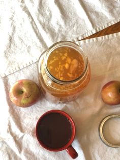 an apple cider and two cups of coffee on a white tablecloth next to some apples