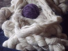 two balls of yarn sitting on top of a pile of white and purple yarns