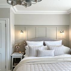 a bed with white linens and pillows in a bedroom next to a wall light