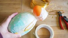 a person is holding an egg in a plastic bottle next to scissors and other crafting supplies