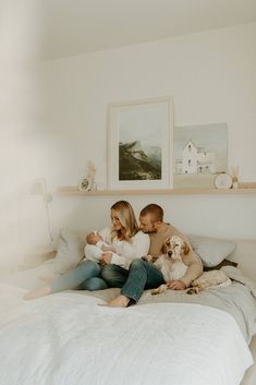 a man and woman are sitting on a bed with two dogs in front of them