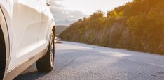 the back end of a white car driving down a road