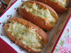 three hot dogs with cheese on them in a red and white tray sitting on a table