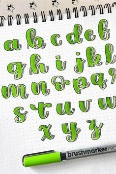 the letters are drawn in green ink on a notepad with a pen next to it