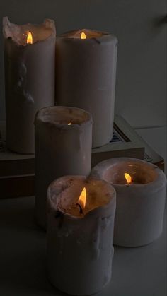 four lit candles sitting on top of a white table next to a book and remote control