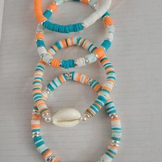 several different colored beads and shells on a sheet of lined paper with an orange, white, and blue beaded necklace