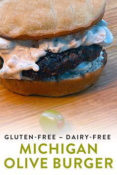 a close up of a burger on a wooden table with the words gluten - free dairy - free michigan olive burger