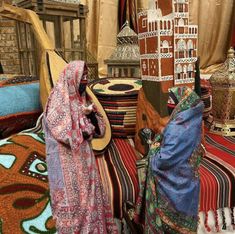 two women are standing in front of some colorful rugs and other decorative items on display