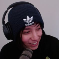 a woman wearing headphones and a beanie smiles while holding a microphone in front of her