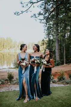 three women standing next to each other in front of a lake