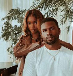 a man and woman sitting next to each other in front of a potted plant