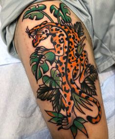 an orange and black tattoo on the leg of a person with green leaves around it