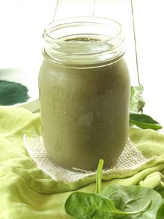 a green smoothie in a glass jar on top of a towel next to some leaves