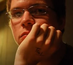 a man with glasses and a tattoo on his left hand is looking at the camera