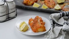 a white plate topped with food next to a baking pan filled with lemon wedges