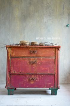 an old red dresser with two bowls on it's top, against a gray wall