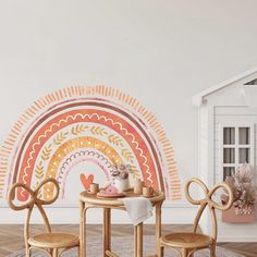 two chairs and a table in front of a wall with a rainbow painted on it