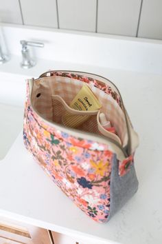 an open purse sitting on top of a white counter next to a sink and faucet