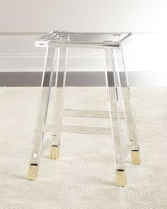 a clear stool with gold legs on carpeted floor