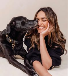 a woman sitting on the floor with her dog and kissing her face in front of her