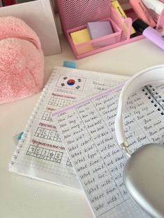 a pink teddy bear sitting on top of a table next to some writing paper and headphones