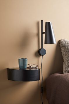 a wall lamp next to a table with a cup on it and a pair of glasses