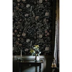 a vase with flowers on a table in front of a floral wallpapered room